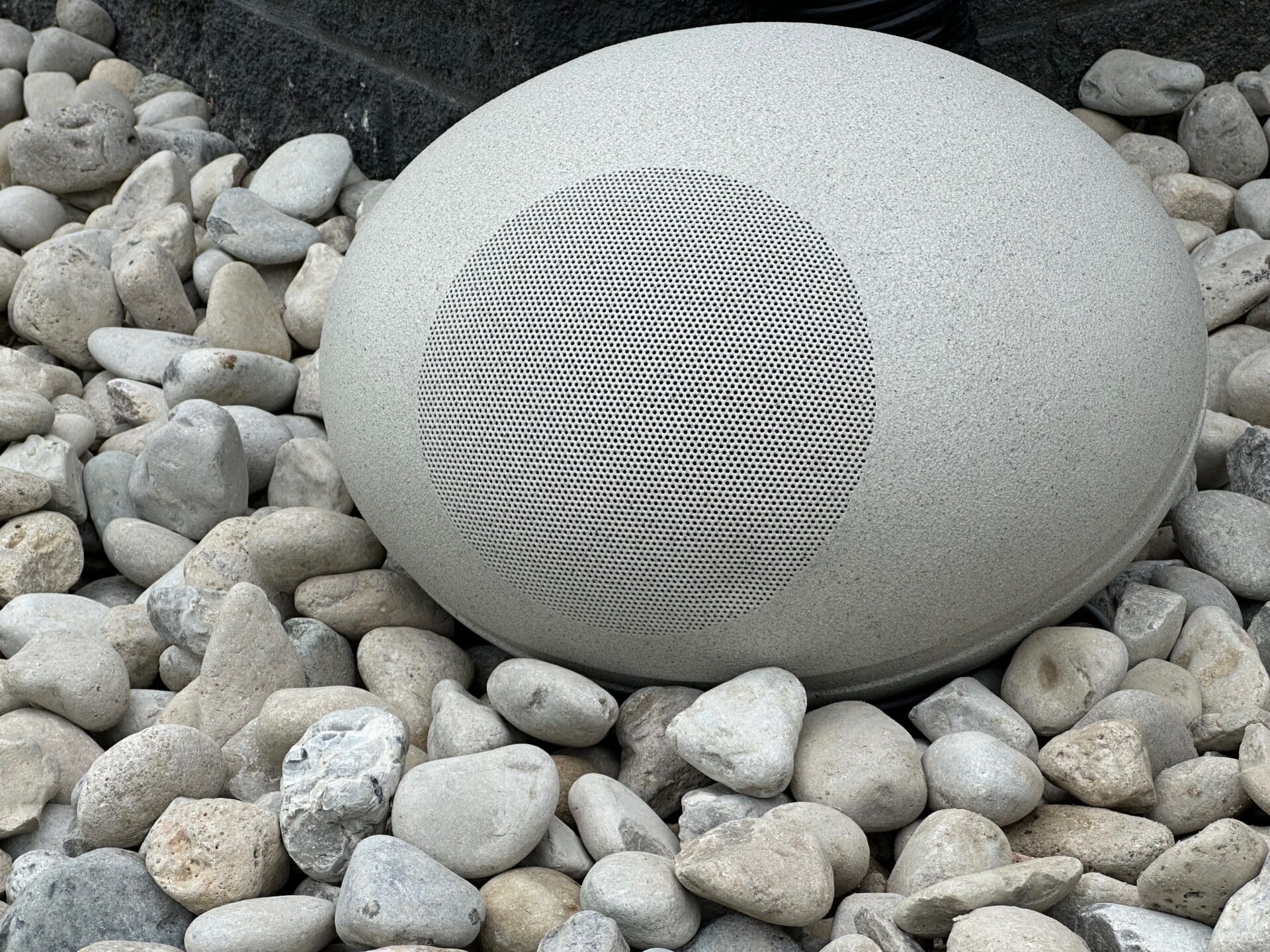 Stylish outdoor speaker on pebbles.